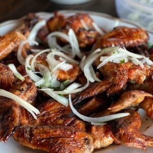 Close-up of mouthwatering grilled chicken wings garnished with fresh onions on a plate.