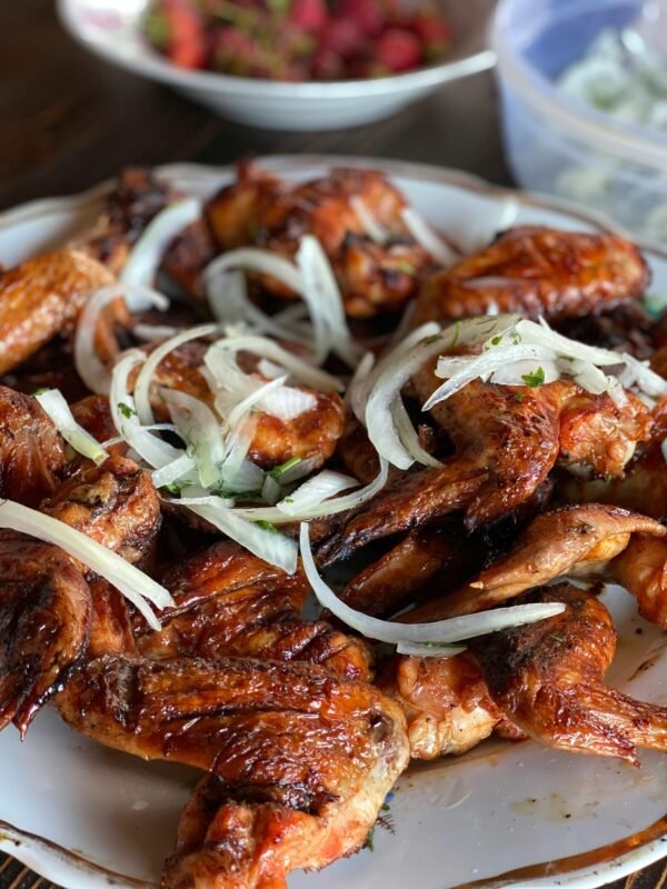 Close-up of mouthwatering grilled chicken wings garnished with fresh onions on a plate.