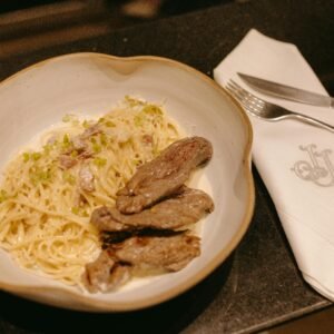 Delicious creamy pasta served with grilled meat on a dining table setting.