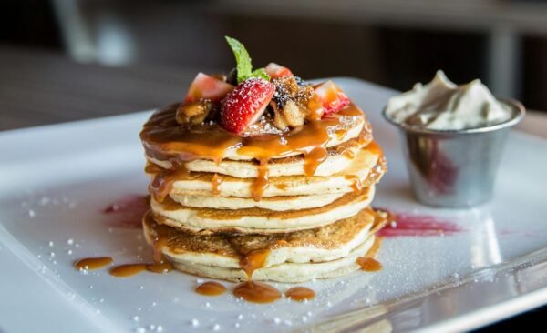 Mouthwatering pancakes with strawberries, nuts, and syrup on a plate.