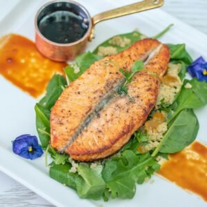 Savor this gourmet salmon served with quinoa, spinach, and a rich sauce on a white plate.