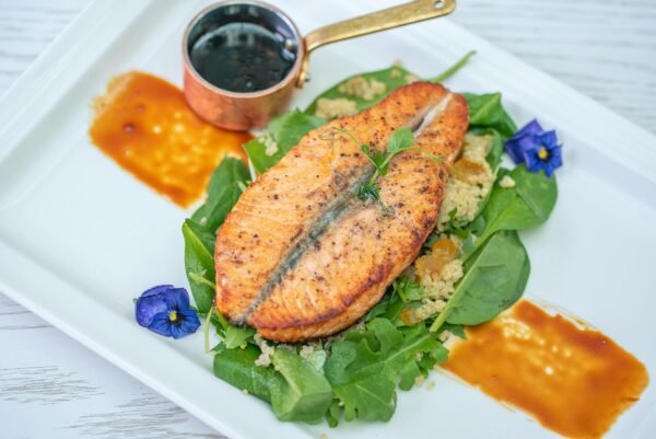 Savor this gourmet salmon served with quinoa, spinach, and a rich sauce on a white plate.